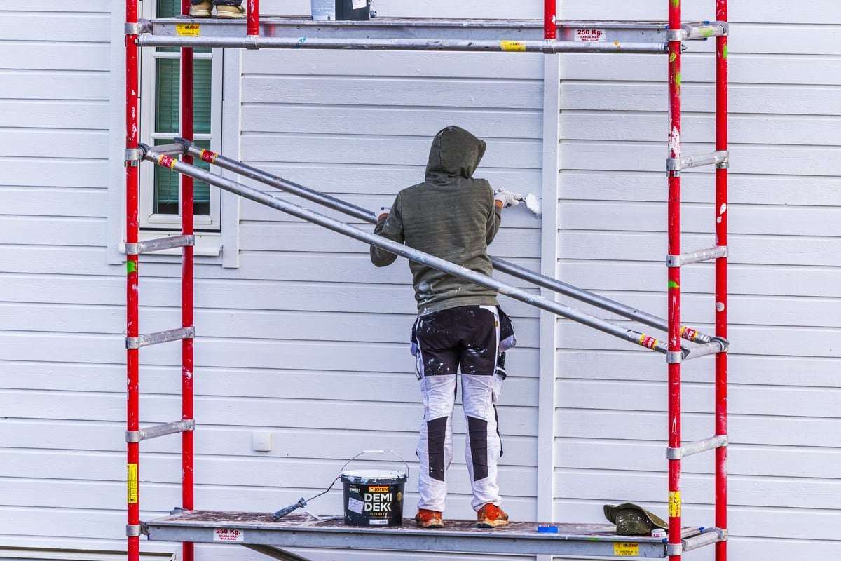 Worker painting the exterior wall of a house from metal scaffolding