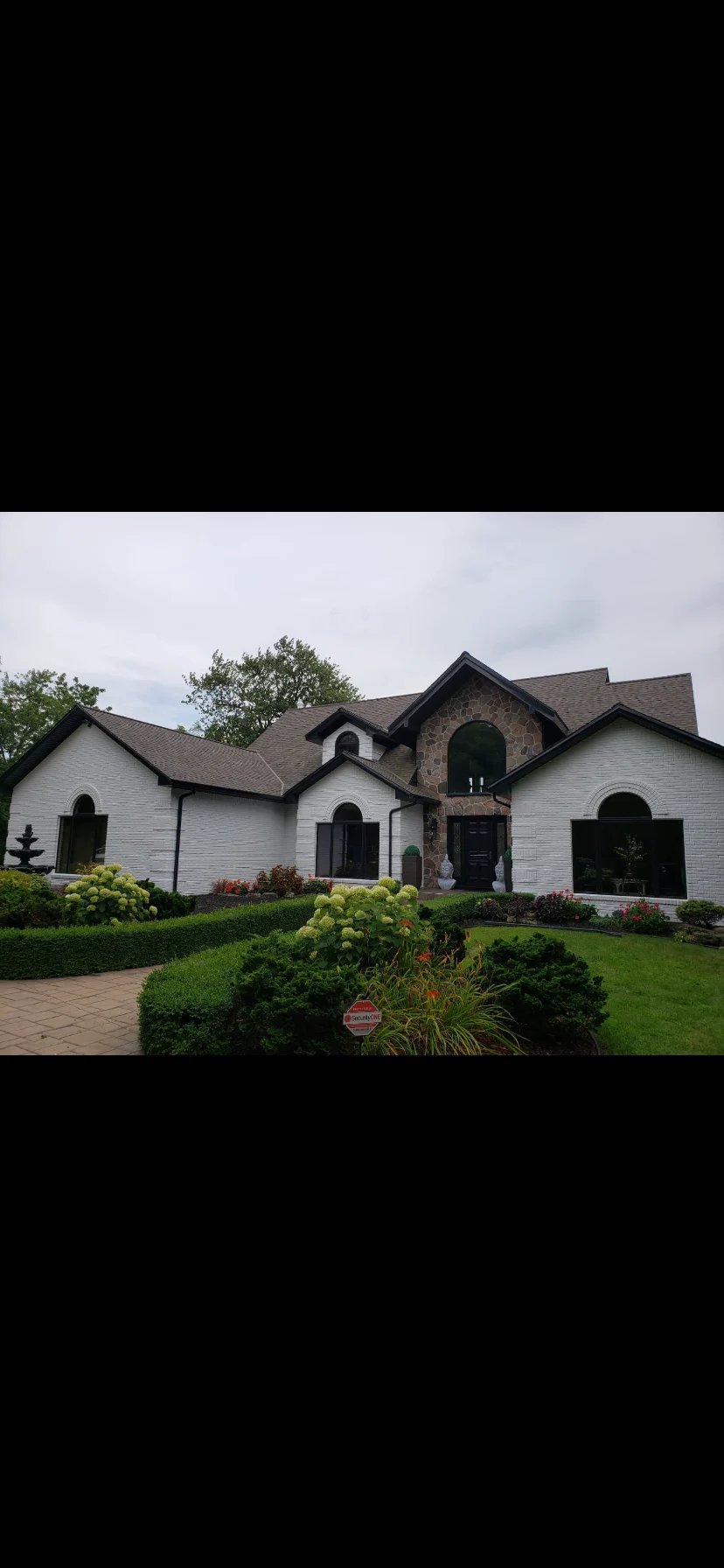 Modern white brick house with arched windows, brick tower detail, manicured landscaping, and brick driveway under cloudy sky