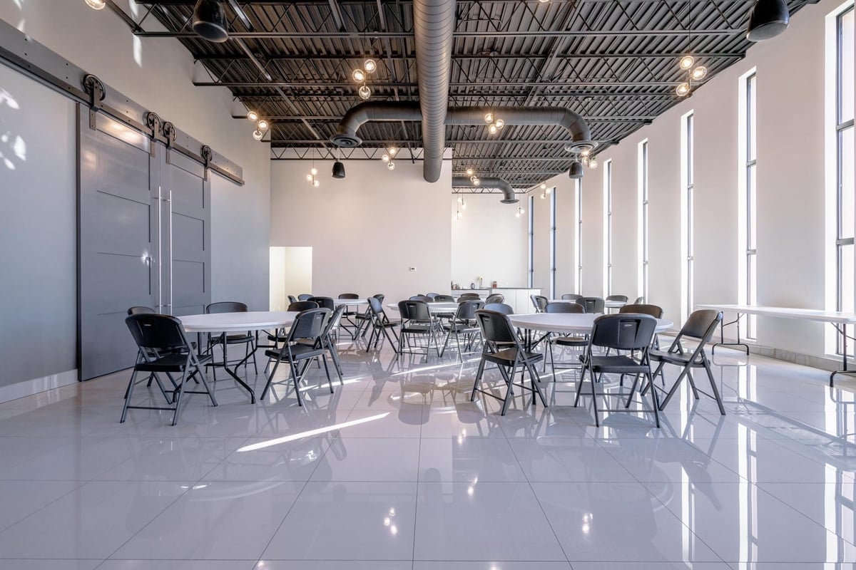 Modern, minimalist office meeting room with polished white floors, floor-to-ceiling windows, industrial ceiling, and contemporary black furniture