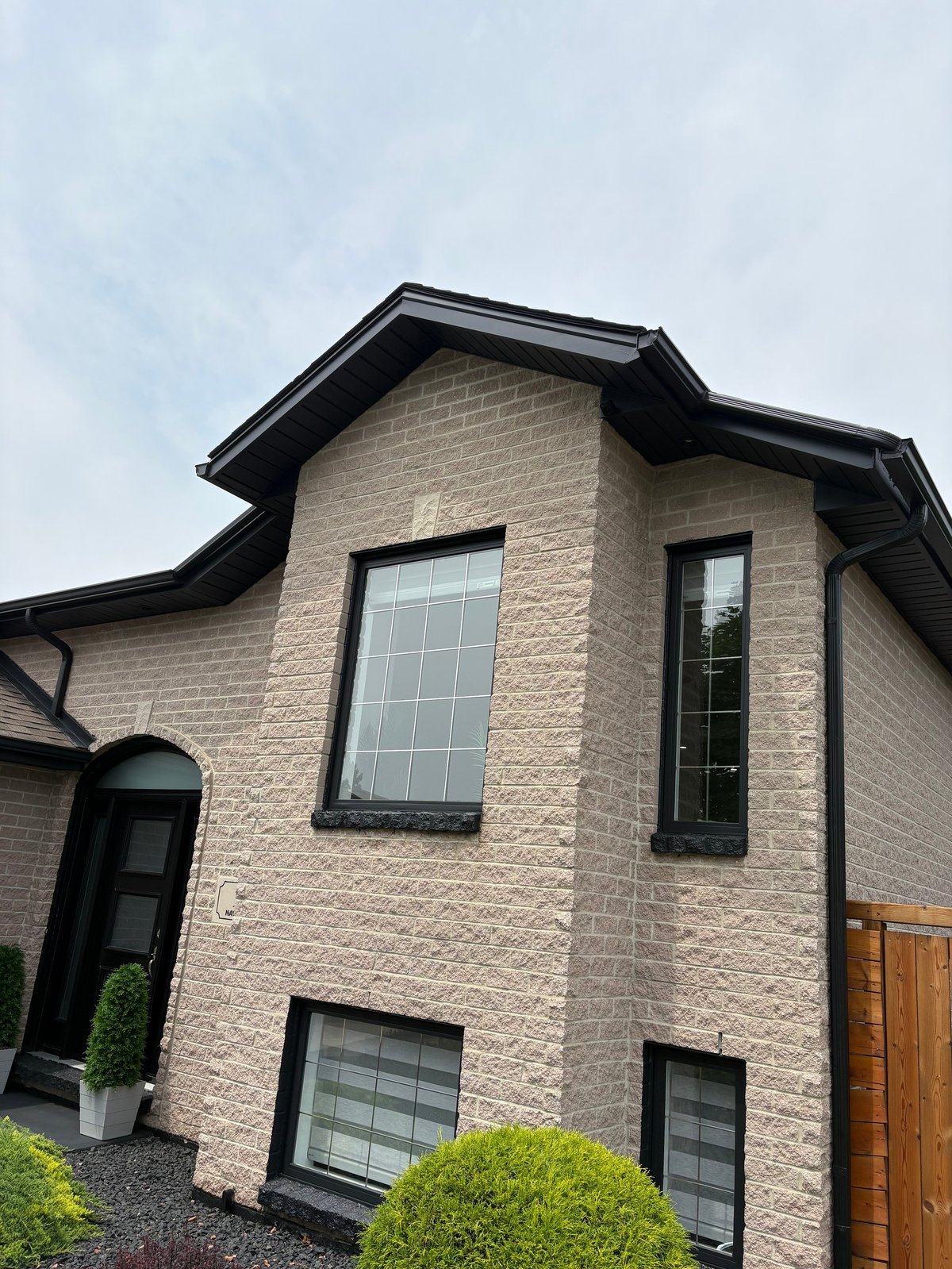 Modern two-story brick house with black trim, large windows, black front door, and manicured shrubs in the front yard