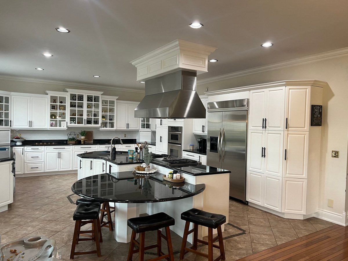 Modern luxury kitchen with white cabinetry, stainless steel appliances, large island with seating, and professional stove hood