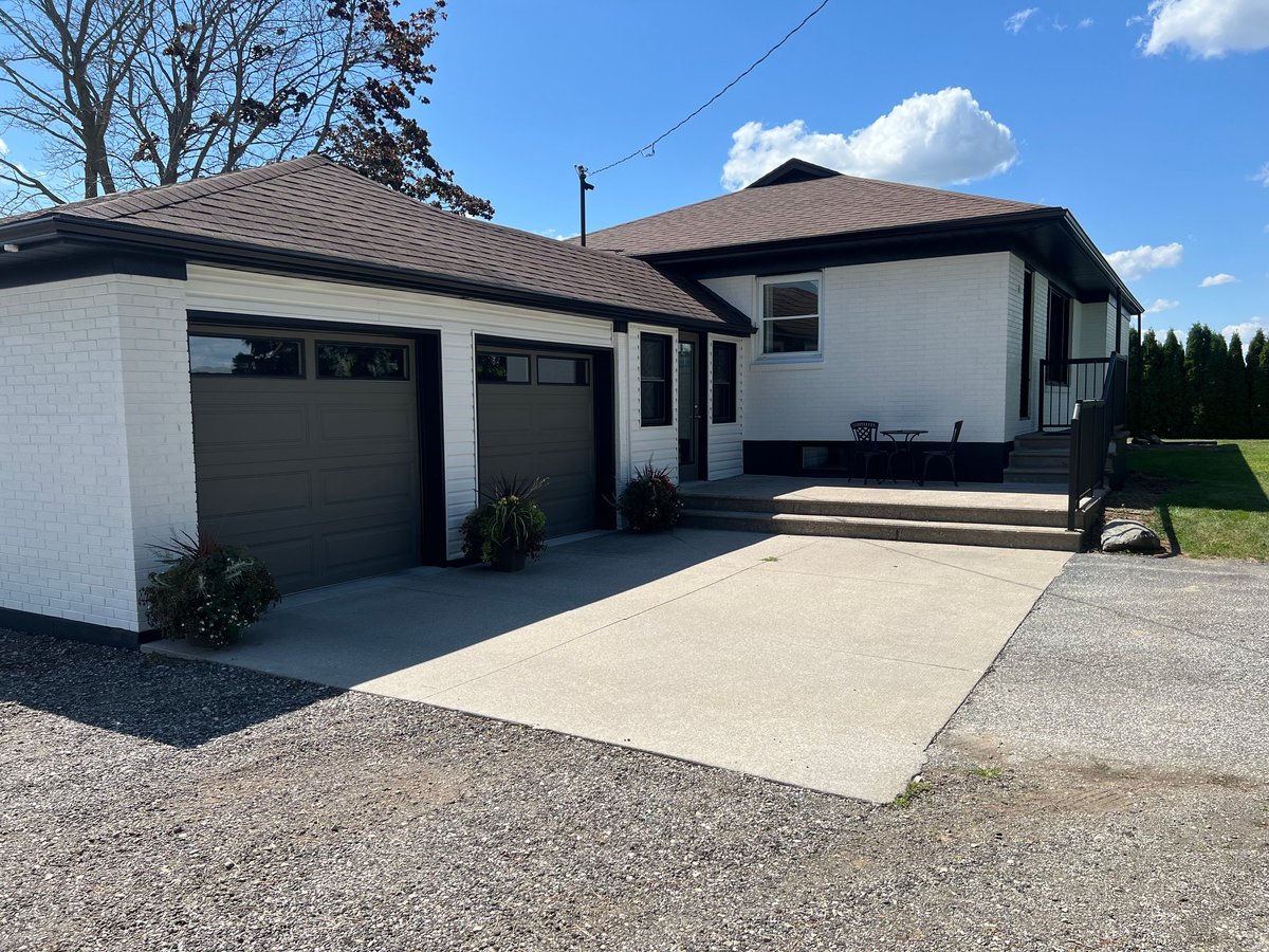 Modern white house with dark roof, double garage, concrete driveway, and front porch on a sunny day